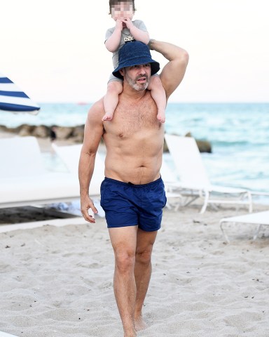 Fresh off hosting New Year's Eve with Anderson Cooper on CNN, Andy Cohen shows off his chiseled torso as he walks shirtless on the beach in Miami with his 10 month-old son Benjamin on his shoulders. The creator of the Real Housewives franchise, is also seen with his personal trainer. *SPECIAL INSTRUCTIONS*** Please pixelate children's faces before publication.***. 02 Jan 2020 Pictured: Andy Cohen; Benjamin Cohen. Photo credit: MEGA TheMegaAgency.com +1 888 505 6342 (Mega Agency TagID: MEGA576898_025.jpg) [Photo via Mega Agency]