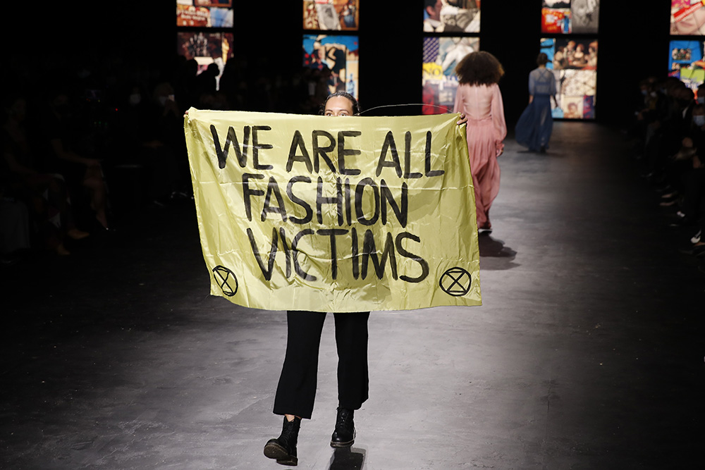 An activist displays a banner during Dior's Spring-Summer 2021 fashion collection presented Tuesday, Sept. 29, 2020 during the Paris fashion week. (AP Photo/Francois Mori)