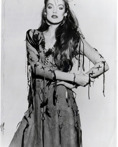 Jerry Hall Wearing Nut Brown Chamois Leather Dress Laced At The Front Trimmed In Blanket Stitch Purple Ribbons And Feathers A65 By Peter Golding. Beaded And Feathered Headband A5. Beaded Bracelets A1.50 All From Ace. 
Jerry Hall Wearing Nut Brown Chamois Leather Dress Laced At The Front Trimmed In Blanket Stitch Purple Ribbons And Feathers A65 By Peter Golding. Beaded And Feathered Headband A5. Beaded Bracelets A1.50 All From Ace.