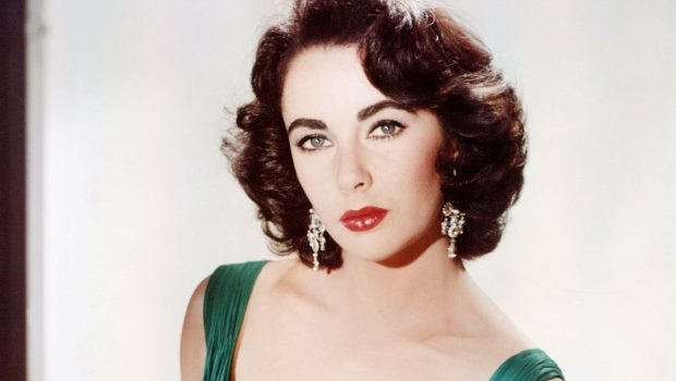 Elizabeth Taylor (1932-2011), British actress, wearing a green sleeveless low-cut dress, with a white fur wrap on the arm of the armchair in which she sits, circa 1950. (Photo by Silver Screen Collection/Getty Images)