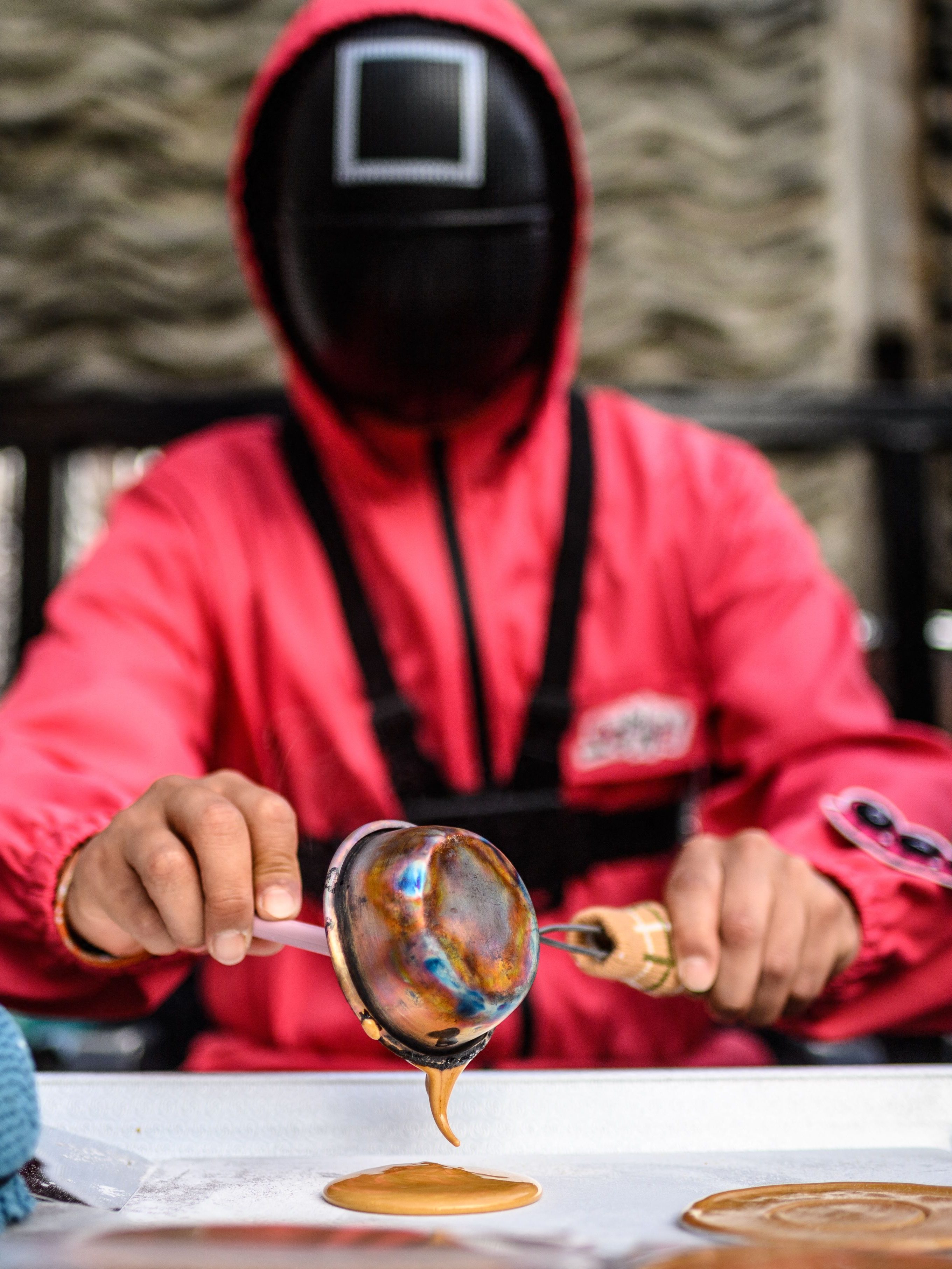 A man dressed as a character from Netflix sensation "Squid Game" makes a crisp sugar candy called a dalgona, the traditional local children's treat featured in the global cultural phenomenon, at his stall in Seoul on November 4, 2021. (Photo by Anthony WALLACE / AFP) (Photo by ANTHONY WALLACE/AFP via Getty Images)