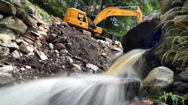 The Dudleyville Pond Dam was taken down by heavy construction equipment after an emergency order because of a high risk of failure. Water poured from a culvert in the dam as it was being removed. (Photo by John Tlumacki/The Boston Globe via Getty Images)